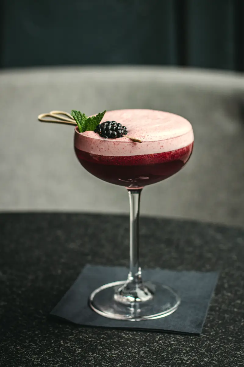 Drink rosado com espuma e amora em taça coupe