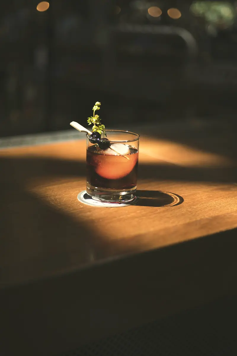 Drink com amora em copo baixo iluminado por um feixe de luz sobre a mesa