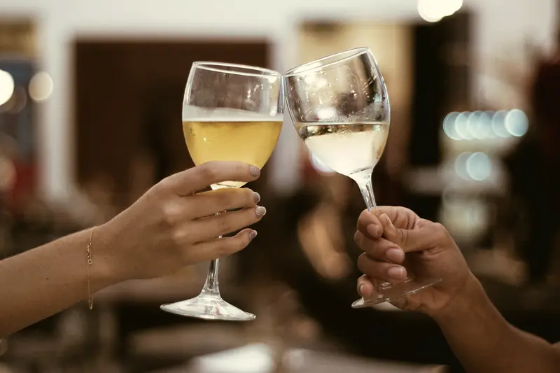 Duas pessoas brindando com taças de vinho branco