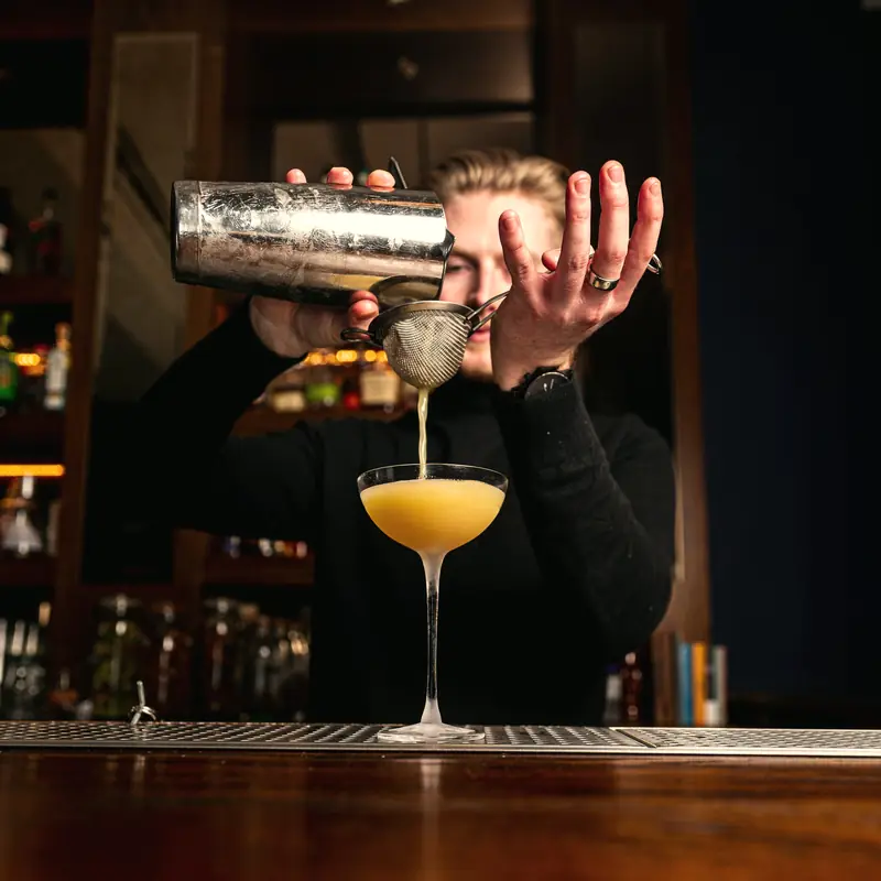 Bartender coando um drink da coqueteleira para uma taça coupe